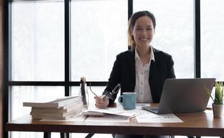 encantadora mujer asiática que trabaja en la oficina usando una laptop mirando la cámara. foto