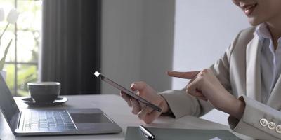 Closeup hand of young woman reading on smartphone and working on laptop computer, online working at home, freelancer using phone with social media, business and communication concept. photo