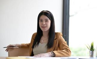 Charming Asian businesswoman working with a laptop at the office. Looking at camera. photo