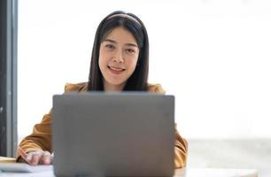 Charming Asian woman working at the office using a laptop Looking at the camera. photo