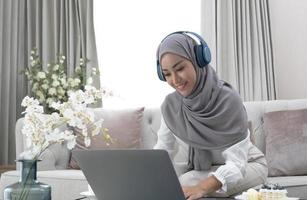 Online Tutoring. Young muslim woman teacher having video call with students, talking at laptop camera, sitting on couch at home photo