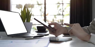 Cropped shot of female blogger searches information on internet websites, uses portable laptop with blank copy screen for your advertisment. Modern cell phone in womans hands, selective focus photo