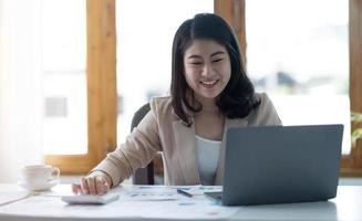 Beautiful young asian woman sitting at coffee shop using laptop. Happy young businesswoman sitting at table in cafe with tab top computer. photo