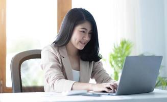 Beautiful young asian woman sitting at coffee shop using laptop. Happy young businesswoman sitting at table in cafe with tab top computer. photo