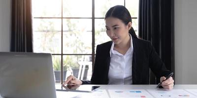 el retrato de una joven mujer asiática independiente está trabajando en su trabajo en una tableta de computadora en una oficina moderna. hacer un informe de análisis contable datos de inversión inmobiliaria, concepto de sistemas financieros y fiscales. foto