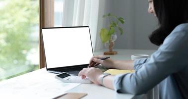Mockup image of a woman using laptop with blank white screen on wooden table in office photo