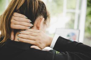 Young asian woman is sitting at work and has pain in her neck photo