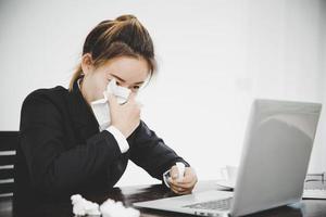 mujer de negocios asiática joven enferma sentada sola en el trabajo estornuda foto