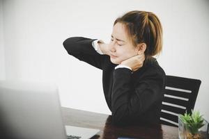 Young asian woman is sitting at work and has pain in her neck photo