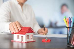 Businesswoman choosing mini house model from model on wood table photo