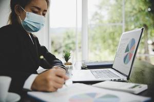asian business woman wearing facial mask working on laptop photo