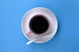 An isolated black coffee on light pink cub on blue background with white spoon photo