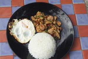 Basil, chicken, fried egg, Thai food The house style is not upscale in a black ceramic plate placed on a plaid concrete table. Ready to serve and delivery photo