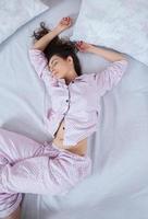 chica duerme en una cama blanca en casa. mujer joven durmiendo en ropa de dormir en el lino blanco en la cama en casa, vista superior. foto