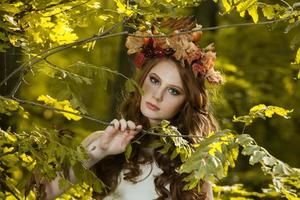 mujer joven sosteniendo un montón de hojas de arce amarillas. retrato de otoño de mujer joven. chica pelirroja en el bosque de otoño foto