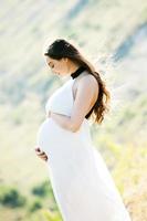 Pregnant woman with long healthy hair and flowers. Beautiful girl waiting for the baby. Future mother hugs her tummy. photo