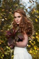 mujer joven sosteniendo un montón de hojas de arce amarillas. retrato de otoño de mujer joven. chica pelirroja en el bosque de otoño foto