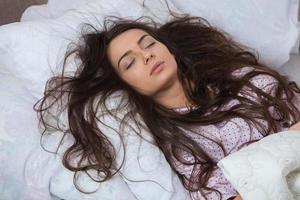 Girl sleeps in a white bed at home. Young woman sleeping in sleepwear on the white linen in bed at home, top view. photo