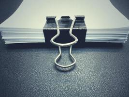 The black clip, white paper clip. Placed on a black surface with dark edges of the desk. photo