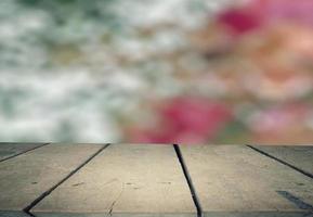 Old plank with blurry red-pink floral background. Used as a counter to place products for presentations and advertisements. photo