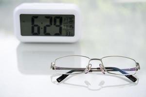 Eye glasses and Digital clock on table at home photo