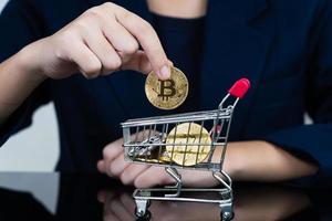 mujer sosteniendo algunas piezas de token bitcoin dorado en carrito de compras foto