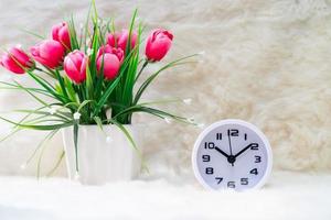 White alarm clock and flower in vase on table photo