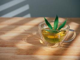 A glass of hot marijuana tea on the wooden table. Cannabis herbal tea with green leaf. photo