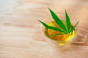 A glass of hot marijuana tea on the wooden table. Cannabis herbal tea with green leaf. photo