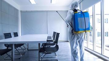 trabajador en equipo de protección personal traje de limpieza en edificio con agua desinfectante en aerosol para eliminar covid 19 foto