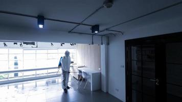 trabajador en equipo de protección personal traje de limpieza en edificio con agua desinfectante en aerosol para eliminar covid 19 foto