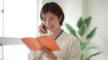 en kvinnlig anställd som öppnar en anteckningsbok medan han pratar i telefon video