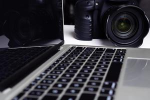 A black digital camera and a computer laptop on a table. photo