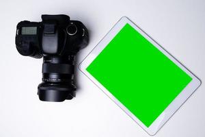 Top view of a black digital camera and a blank screen tablet on a table. photo