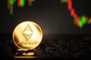 A golden coin with ethereum symbol on computer keyboard with stock graph background. photo