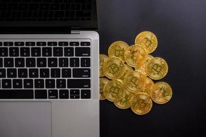 Computer and golden coins with bitcoin symbol on a black background. photo