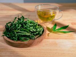 A glass of hot marijuana tea on the wooden table. Cannabis herbal tea with dried leaves photo