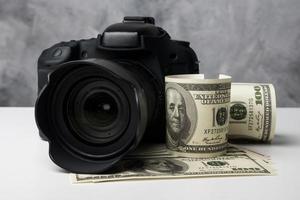 una cámara digital negra y billetes en una mesa blanca con fondo grunge. foto