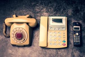 un teléfono antiguo con dial rotatorio, un teléfono fijo y un celular obsoleto en un fondo grunge. foto