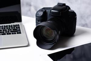 A black digital camera, a tablet and a computer laptop on a table. photo