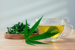 A glass of hot marijuana tea on the wooden table. Cannabis herbal tea with dried leaves photo