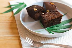 Homemade sweetmeat with marijuana or cannabis leaf on white plate. Alternative medicine concept. photo