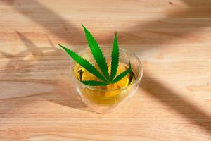 A glass of hot marijuana tea on the wooden table. Cannabis herbal tea with green leaf. photo