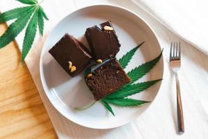 Homemade sweetmeat with marijuana or cannabis leaf on white plate. Alternative medicine concept. photo