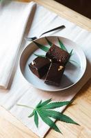 Homemade sweetmeat with marijuana or cannabis leaf on white plate. Alternative medicine concept. photo