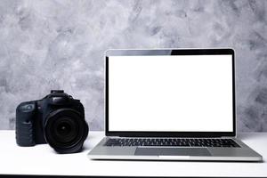 A black digital camera and a computer laptop on a table photo