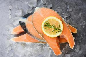 Close up of raw salmon fish fillet and ice - Fresh raw salmon steak with herbs rosemary on black plate background photo