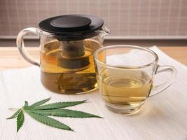 A glass of hot marijuana tea on the table. Cannabis herbal tea with dried leaves. Alternative medicine concept. photo