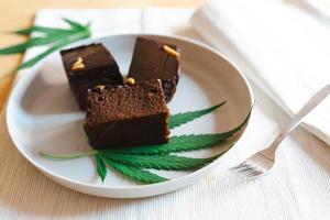 Homemade sweetmeat with marijuana or cannabis leaf on white plate. Alternative medicine concept. photo