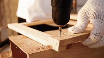 primer plano de carpintero usando taladro para atornillar piezas de tablero en el sitio.